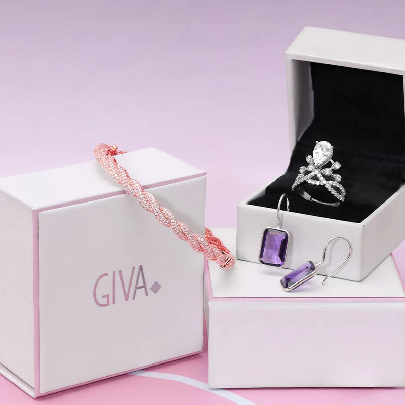 A GIVA gift box with a rose-gold bracelet, silver ring and amethyst earrings on a soft pink background