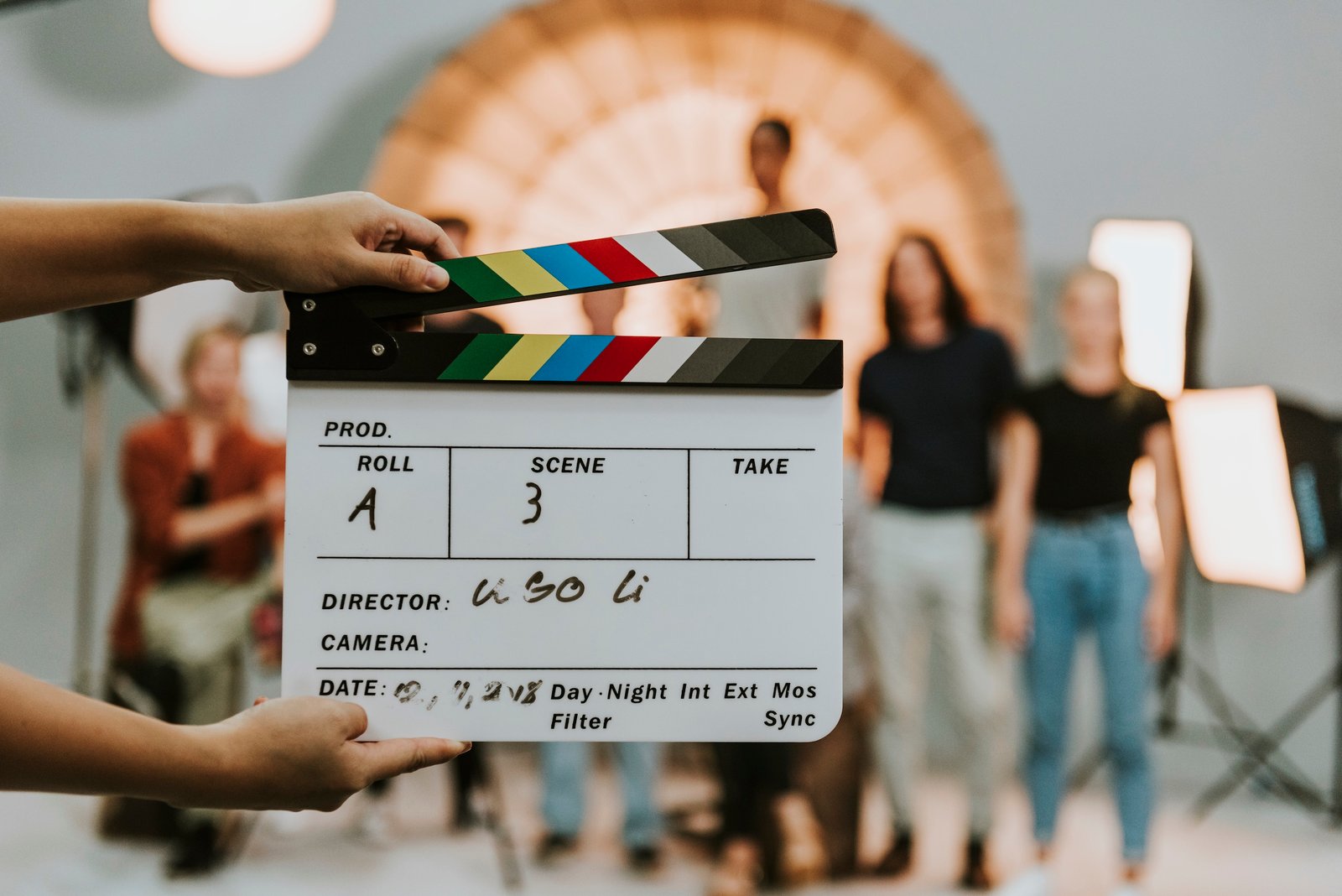 A clapperboard held up on a film set with production crew visible in the background